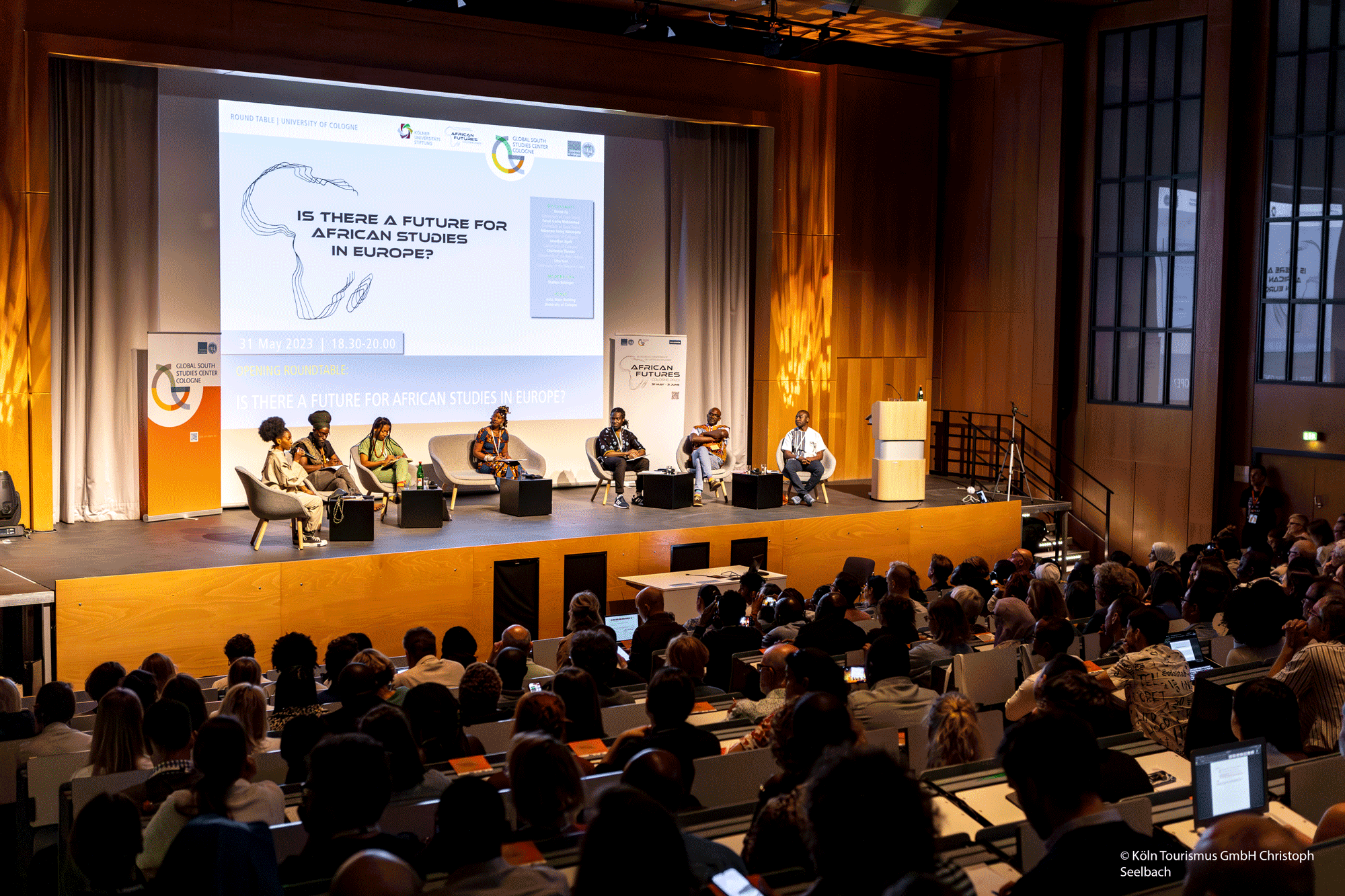 Picture of a full auditorium with a group of panelists sitting on a stage. The picture depicts the ECAS 2023 opening roundtable
